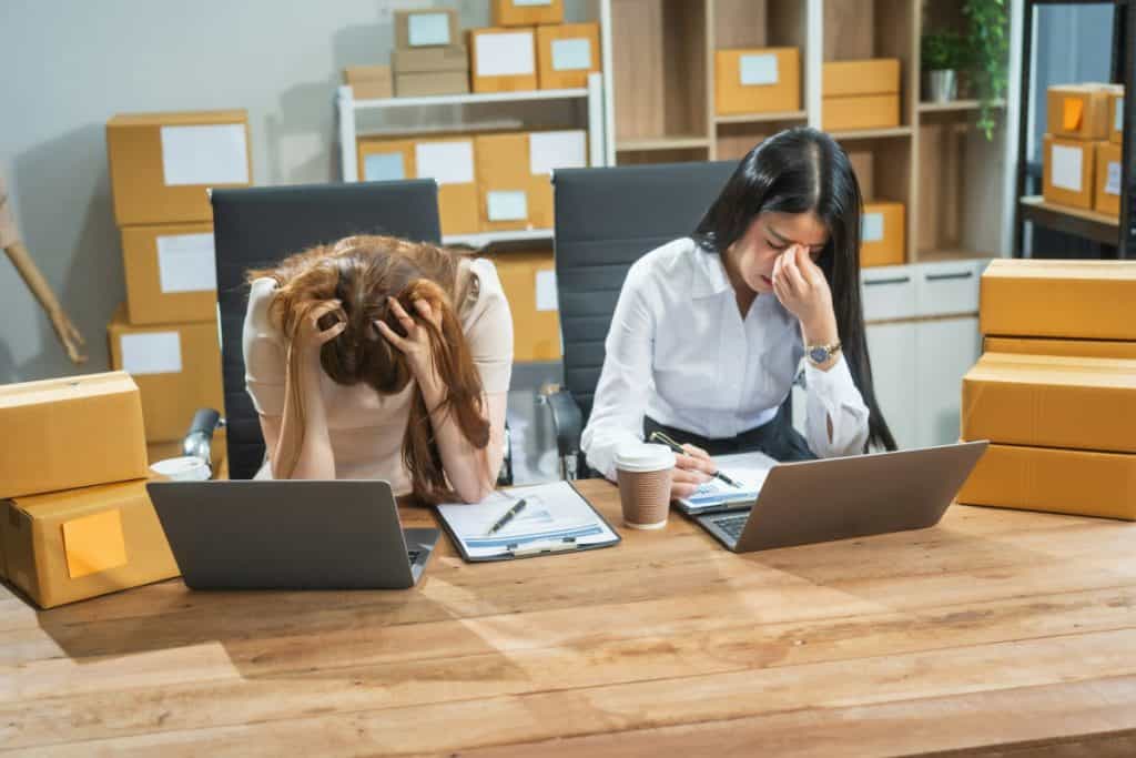 Two Asian business woman work at their desks, stressed by poor sales not reaching targets.Frequent